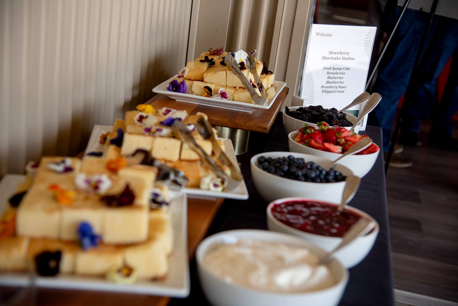 Strawberry shortcake dessert station with fresh sponge cake, strawberries, blueberries, blackberries, whipped cream, and strawberry sauce.