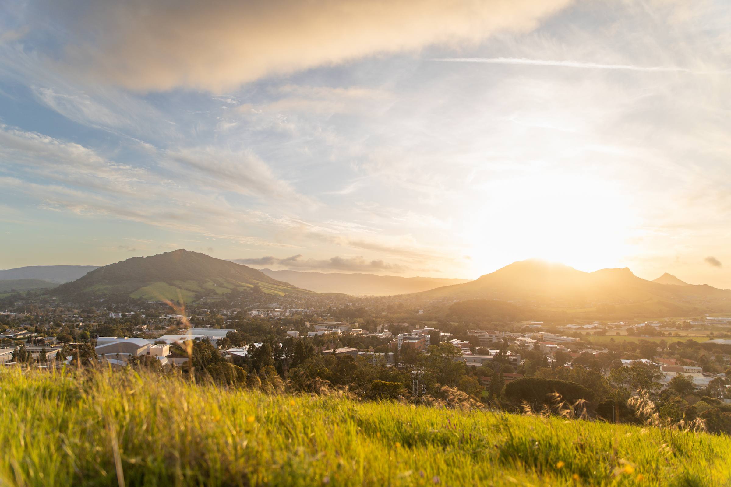 Sunset over San Luis Obispo, California, with rolling green hills and the Cal Poly campus in the foreground beneath a colorful sky.
